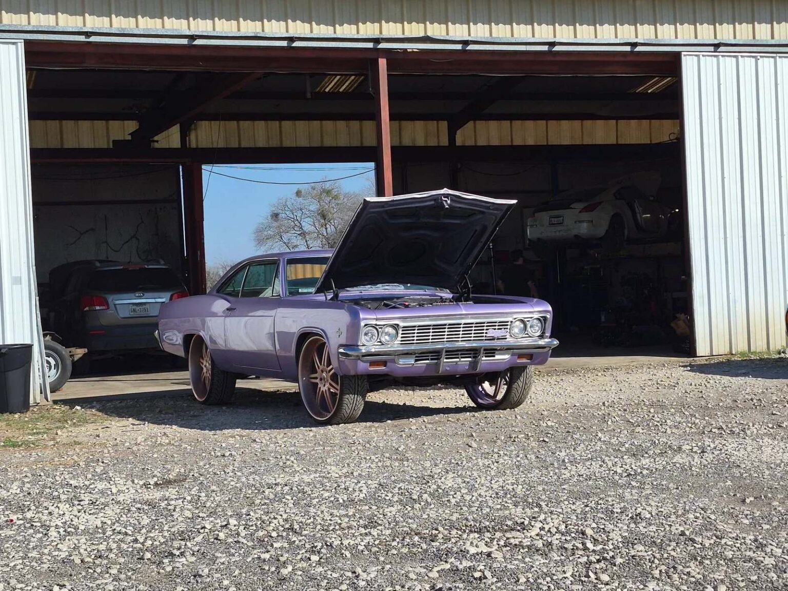 Roy&rsquo;s Mobile Mechanic HQ shop in San Antonio: a classic Chevrolet Impala parked at the open bay doors with another vehicle raised on a lift inside